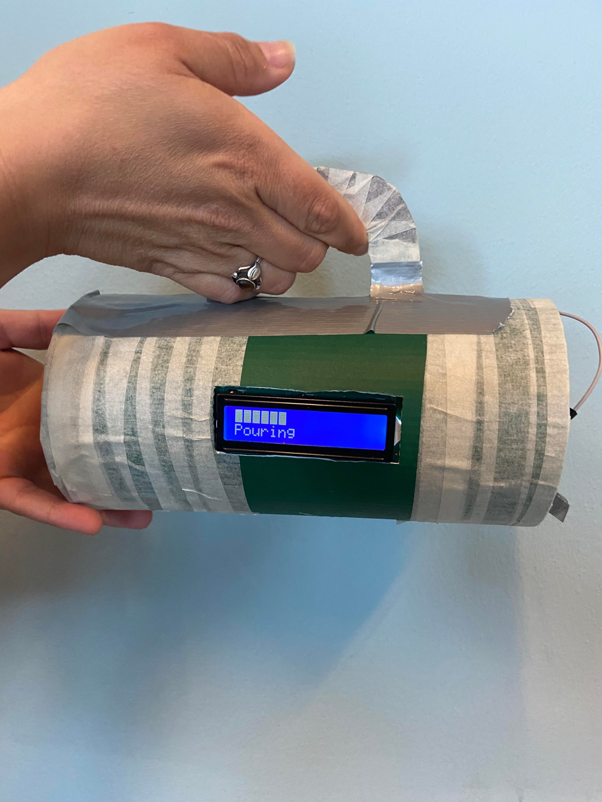 Hånd holder den fysiske CupTask-prototype med displayet i tilstanden Pouring